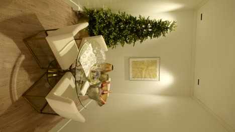 Wide-vertical-shot-of-glass-table-with-drinks-and-Christmas-tree,-handheld