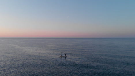Colourful-horizon-sunset-drone-shot-with-one-fishing-boat-surrounded-by-serene-waves,-sunrise-skyline