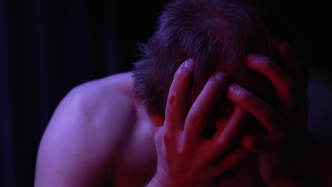shirtless-man-robbing-his-head,-pulling-his-hair,-scratching-his-skin,-confused-and-dazed-in-red-lit-room