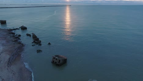 Beautiful-aerial-establishing-view-of-Karosta-concrete-coast-fortification-ruins,-vibrant-high-contrast-sunset-over-calm-Baltic-sea,-winter-evening,-wide-drone-shot-moving-forward,-tilt-up