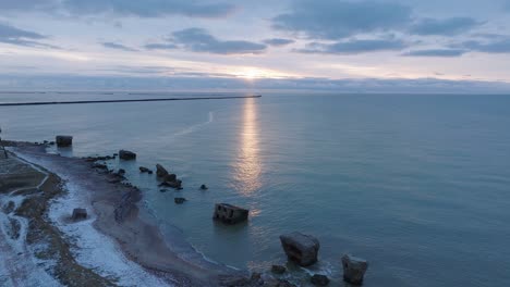 Beautiful-aerial-establishing-view-of-Karosta-concrete-coast-fortification-ruins,-vibrant-high-contrast-sunset-over-calm-Baltic-sea,-winter-evening,-wide-drone-shot-moving-forward-high