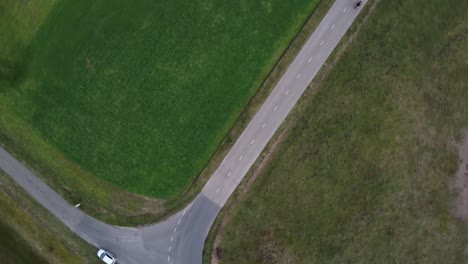 Aerial-drone-shot-of-motorcyclist-driving-down-a-small-farm-road