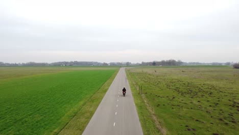 Drone-shot-following-motorcyclist-on-a-small-road-between-grass-fields
