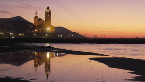 Coastal-sunset-sky-reflected-in-water,-hilltop-silhouette-with-church