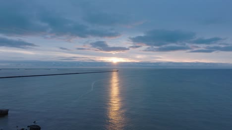Beautiful-aerial-establishing-view-of-Karosta-concrete-coast-fortification-ruins,-vibrant-high-contrast-sunset-over-calm-Baltic-sea,-winter-evening,-wide-drone-shot