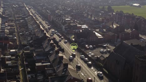 Aerial-view-orbiting-electric-car-charged-symbol-flashing-above-vehicle-driving-long-road-in-British-neighbourhood-at-sunrise