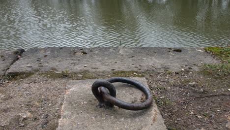 Close-up-of-a-canal-boat-mooring-ring-on-a-dock-next-to-the-river