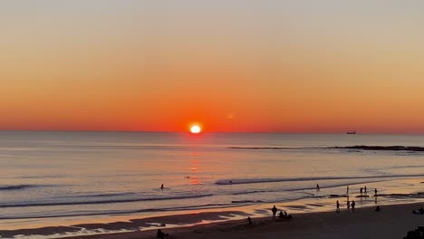 Unglaublich-Schöne-Sonnenuntergangshimmelreflexionen-Der-Wellen-Des-Atlantischen-Ozeans-Am-Strand-Von-Carcavelos,-Boote,-Schiffe-Und-Surfer-Im-Wasser,-Orangefarbene-Blautöne