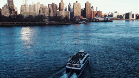 Aerial-view-around-a-ferry-in-front-of-the-Upper-East-Side-cityscape,-spring-sunset-in-NYC,-USA