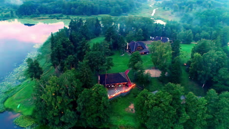 Luxury-countryside,-lakeside-homes-with-lights-illuminating-the-deck-at-dusk---aerial-reveal-of-the-landscape