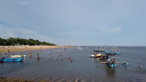 People-Swim-Walk-and-Boats-Sail-in-Sanur-Mertasari-Beach,-Bali,-Indonesia,-Blue-Water-and-White-Sand-in-Afternoon-Warm-Sky,-Island-of-Gods-Travel-and-Tourism