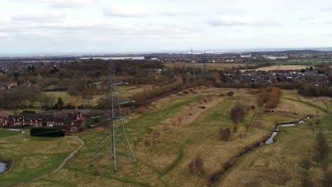 Electricity-distribution-power-pylon-overlooking-British-parkland-countryside,-Hight-to-low-shot