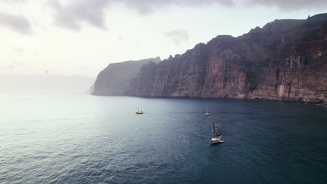 Aerial-view-of-sailboat-float-near-rocky-volcanic-coast-in-Tenerife