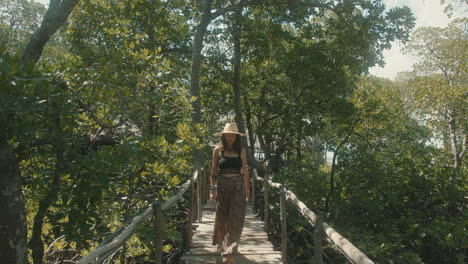 Cámara-Lenta-De-Una-Atractiva-Mujer-Caucásica-Con-Un-Sombrero-De-Paja-Cruzando-Un-Puente-De-Madera-En-Un-Bosque-Verde
