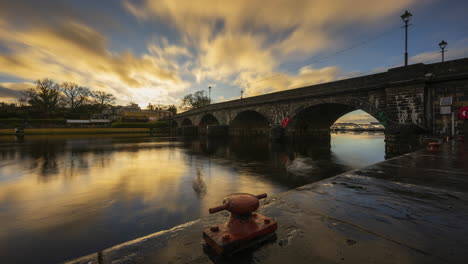 Zeitraffer-Von-Carrick-Auf-Der-Shannon-Town-Bridge-In-Der-Grafschaft-Leitrim-Und-Roscommon-Mit-Verkehr,-Menschen-Und-Bewegten-Abendwolken-Bei-Sonnenuntergang-Am-Fluss-Shannon-In-Irland