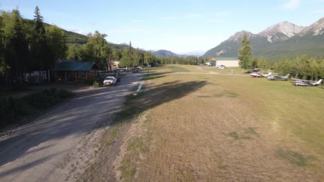 Drone-footage-slowly-flying-over-a-private-grass-runway-with-vehicles-parked-along-the-buildings-in-the-Talkeetna-Mountains