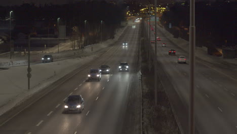 Slow-left-paying-shot-across-a-busy-highway-with-vehicles-traveling-in-both-directions,-snowy-winters-evening
