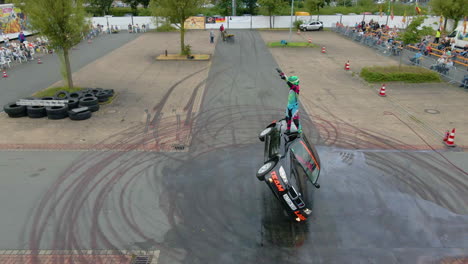 Stuntman-Standing-On-Top-Side-Of-A-Car-Driving-On-Two-Wheels-In-A-Stunt-Show