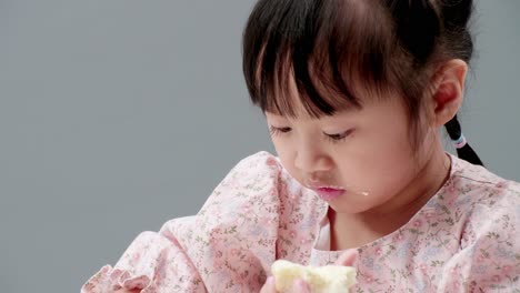 Close-up-of-little-Asian-girl-concentrate-on-food,-smile-and-eat-crispy-butter-toast-happily-at-home