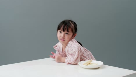 Asiatic-child-eating-piece-of-sweet-in-studio-with-gray-background