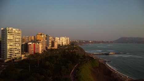 AERIAL---Beach-and-coastline-in-luxurious-Miraflores,-Lima,-Peru,-wide-shot-forward