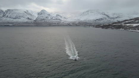 Boat-speeding-along-ocean-in-Arctic,-freezing-hostile-conditions,-drone-fly-over