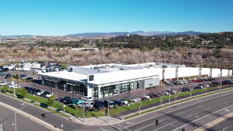 Ascending-aerial-view-of-a-car-dealership-on-an-intersection-with-a-view-of-the-landscape