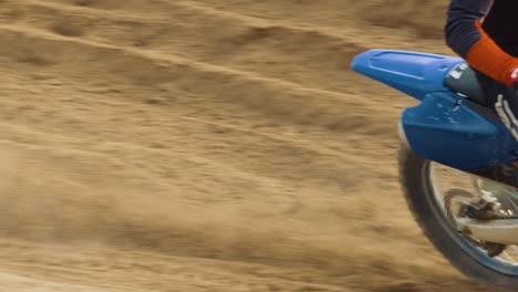 Motocross-rider-comes-into-frame-from-the-left,-spins-the-rear-tire-and-sprays-sand-in-slow-motion