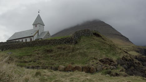 Wide-Tilt-Down-of-a-Church-and-Mountains-in-Vidareidi,-Faroe-Islands
