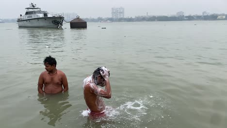 Close-up-view-of-two-men-seen-taking-a-bath-in-the-river-Ganga-at-sunrise-in-Kolkata,-India-with-the-view-of-a-boat-in-the-background