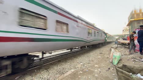 Tren-De-Pasajeros-Con-Un-Motor-Diesel-Que-Transporta-Pasajeros-Que-Pasan-Por-La-Ajetreada-Ciudad-De-Dhaka,-Bangladesh,-En-Una-Mañana-Soleada