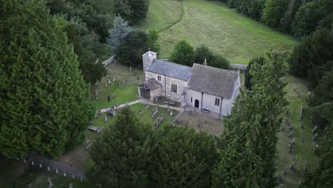 Smooth-aerial-drone-arc-between-tall-conifers,-showing-the-ancient-church-in-setting
