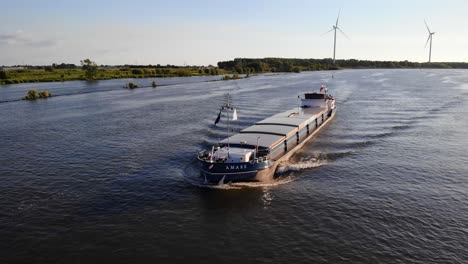 Aerial-Tracking-Shot-Off-The-Forward-Bow-Of-Amare-Inland-Motor-Freighter-Travelling-Along-Against-Still-Wind-Turbines-In-The-Background