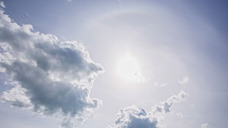 Low-angle-shot-of-sun-halo-ring-surrounding-the-sun-on-dramatic-cloudy-sky-with-white-cumulus-cloud-movement-in-timelapse