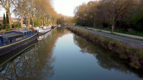 Drone-view-of-the-house-boats-on-the-"Canal-du-Midi"-along-the-city-of-Toulouse,-on-a-sunny-Spring-morning