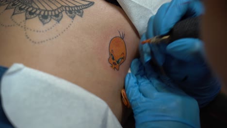 The-tattoo-artist-is-tattooing-Tweety-canary-from-Looney-tunes-on-a-woman's-skin