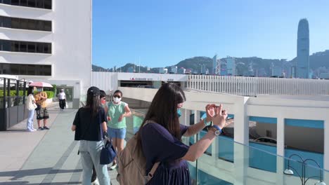 Die-Menschen-Genießen-Ihren-Nachmittag-Am-Hafen,-Während-Sie-An-Einem-Sonnigen-Tag-Fotos-Von-Der-Skyline-Der-Insel-Hongkong-Machen