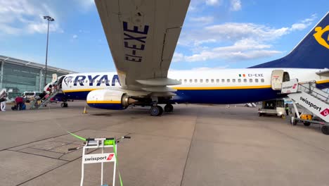 People-boarding-a-Ryanair-airplane-at-an-international-airport-in-Malaga-Spain,-cool-view-from-under-a-big-airplane-wing,-people-going-on-a-holiday,-4K-shot