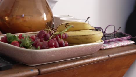 Floating-shot-of-strawberries,-bananas-and-grapes-on-a-tray,-sitting-on-a-side-table