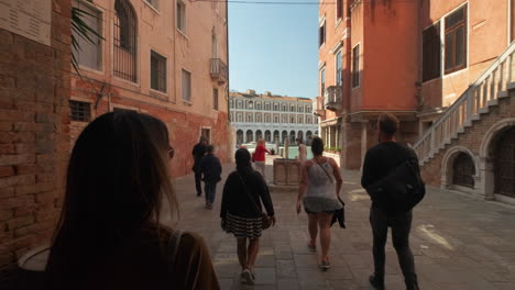 Slow-motion-back-view-showing-group-of-tourists-walking-between-historic-alleys-of-Venice,Italy