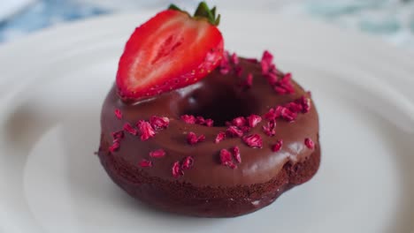 Delicious-chocholate-donut-with-strawberry-and-sprinkles-slowly-rotating-on-white-plate