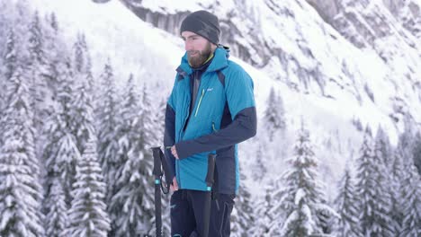 Bearded-skier-man-closes-jacket-in-snow-forest-mountain