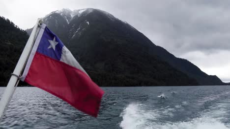 Bandera-Chilena-Ondeando-Con-El-Lago-De-Todos-Los-Santos-Y-Montañas-Cubiertas-De-Nieve-En-El-Fondo