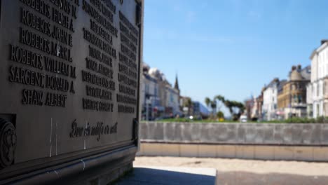 Llandudno-seaside-town-houses-behind-plaque-names-closeup-on-remembrance-war-memorial-on-sunny-promenade-dolly-right