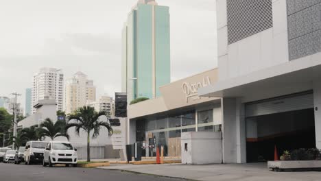 Tilt-down-shot-revealing-Plaza-61-commercial-locals-street-entrance-and-Global-Bank-smart-tower-building-in-the-skyline-background-displaying-Panama-City's-architectural-development