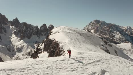 Cinematic-circling-drone-shot-of-hiker-walking-along-a-steep-snowy-ridge