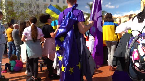 Slow-pan-across-man-wearing-EU-Flag-on-his-back-during-anti-war-protests
