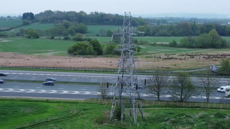 Vehicles-on-M62-motorway-passing-pylon-tower-on-countryside-farmland-fields-aerial-orbit-left-view