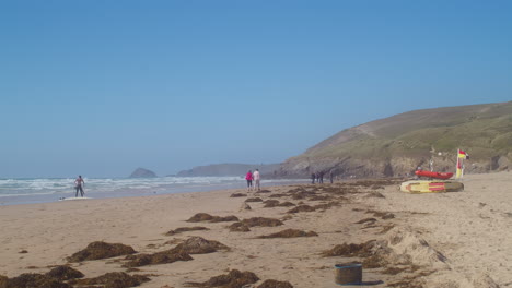 Tourists-At-The-Sandy-Shore-With-Scattered-Seaweed-At-Perranporth-Beach-In-Cornwall,-England---Wide-Shot