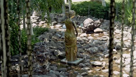 Golden-like-statue-of-lady-in-stream-of-rocks-and-cascading-water-feature